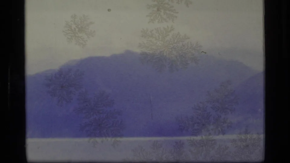 1977 Alaska 8mm frame with a lake, layered purple mountain ridge, pale sky, haze, and frost-like film marks.