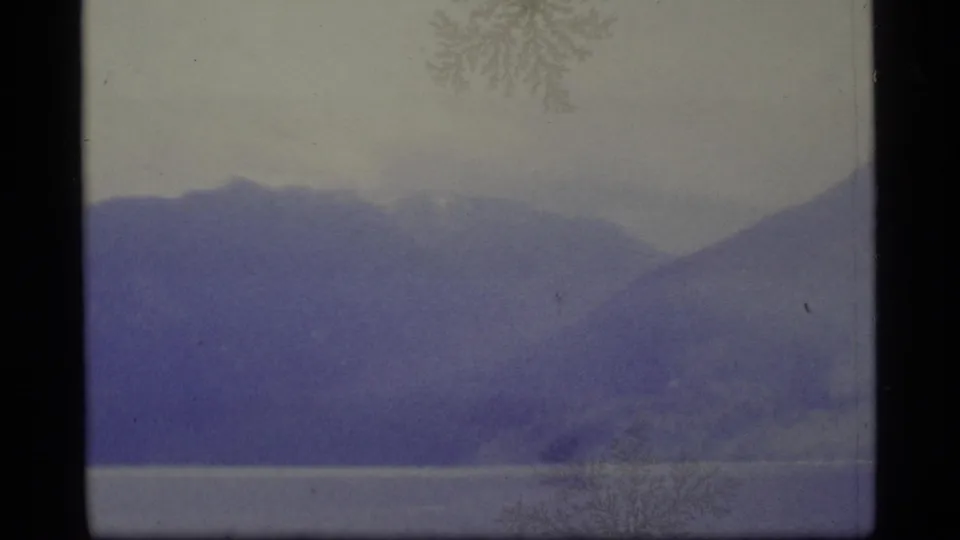 1977 Alaska 8mm frame showing distant mountains beyond a lake, with haze, faded color, and visible film wear.