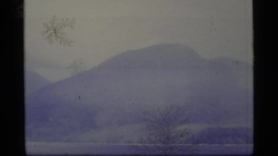 1977 Alaska 8mm frame showing blue-purple hills across a still lake, with a sparse tree silhouette near the shore.
