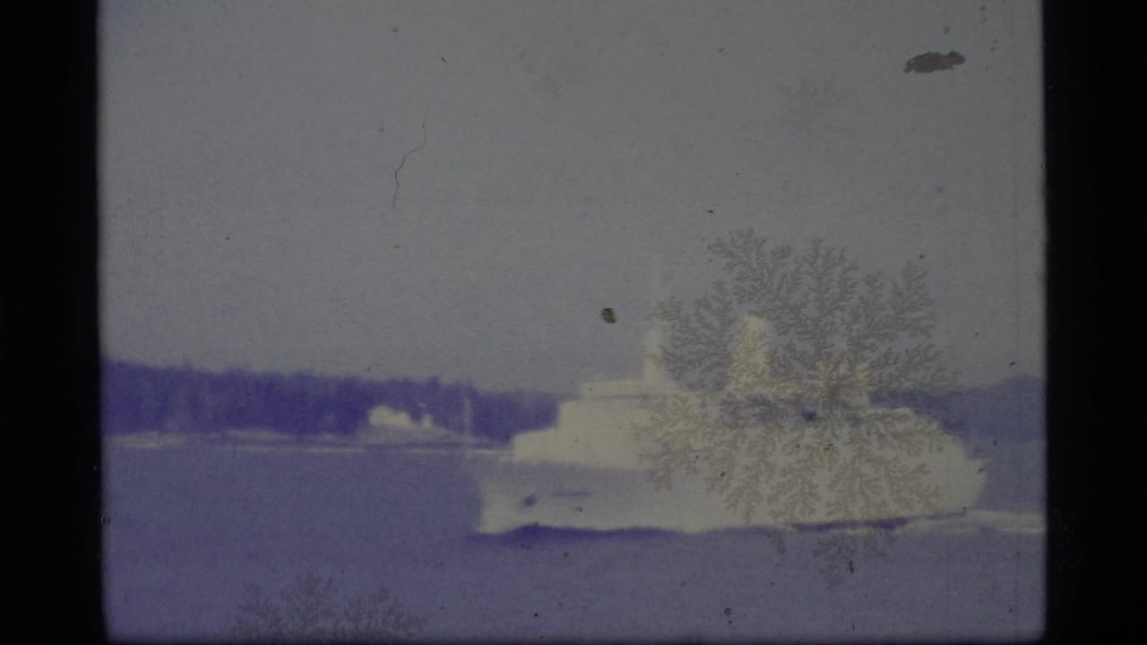 White passenger ship crossing calm water with a distant shoreline and film artifacts.
