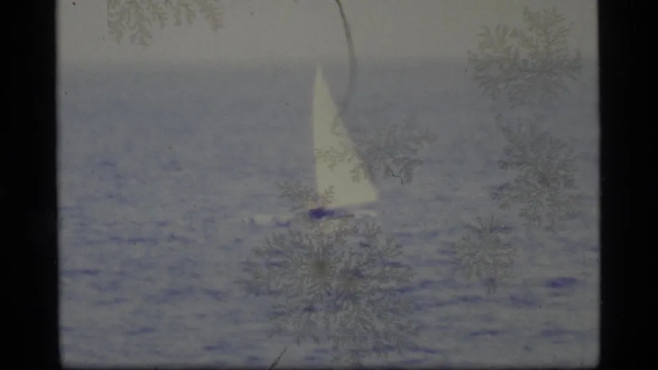 1977 Alaska 8mm frame showing a small sailboat with a bright white sail moving over rippled water, partly obscured by film artifacts.