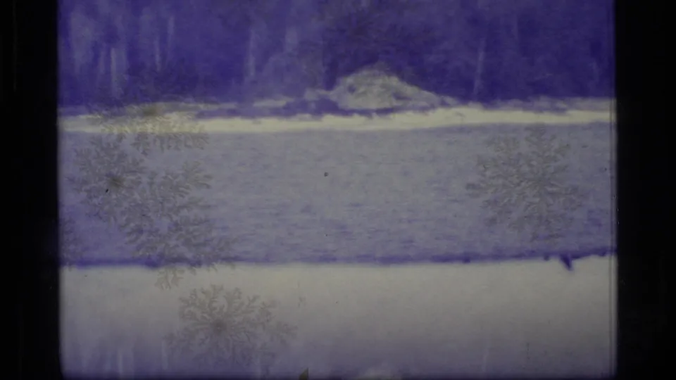 Faded 1977 Alaska 8mm view of water, distant trees, shoreline rocks, and surface marks from the film scan.