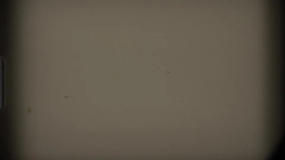 Mostly blank 8mm frame showing tan film density, dark edge shadowing, dust, and faint surface marks.