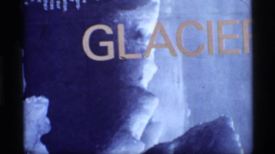 1977 Glacier Bay 8mm title-card frame with large GLACIER letters over blue-toned icy texture and visible film grain.