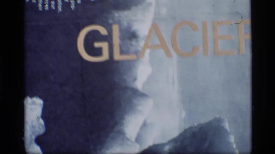 1977 Glacier Bay 8mm frame with partial GLACIER lettering, pale blue title-card texture, grain, and dark vertical border.