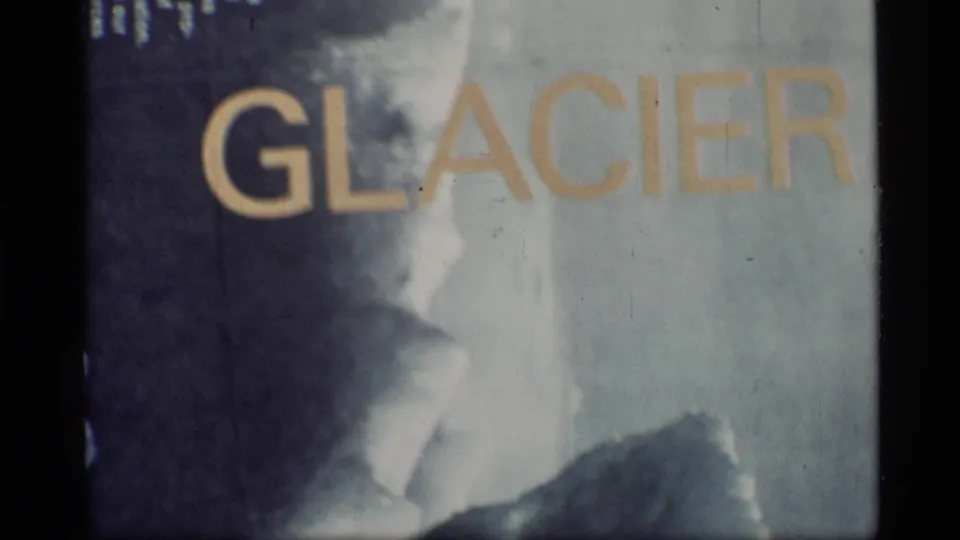 1977 8mm frame from Glacier Bay, Alaska showing partial yellow GLACIER lettering over a soft icy-looking backdrop.