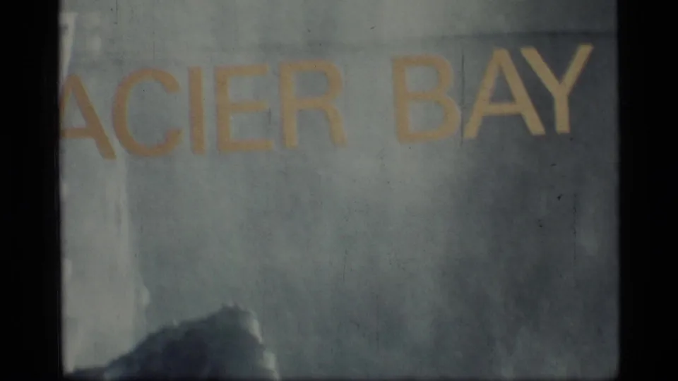 Close 8mm view of the Glacier Bay sign in Alaska, with yellow place-name text and visible archival film texture.