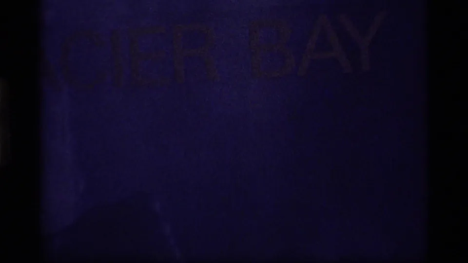 Purple-shifted 8mm frame where the Glacier Bay title is faintly visible under dark exposure and heavy grain.