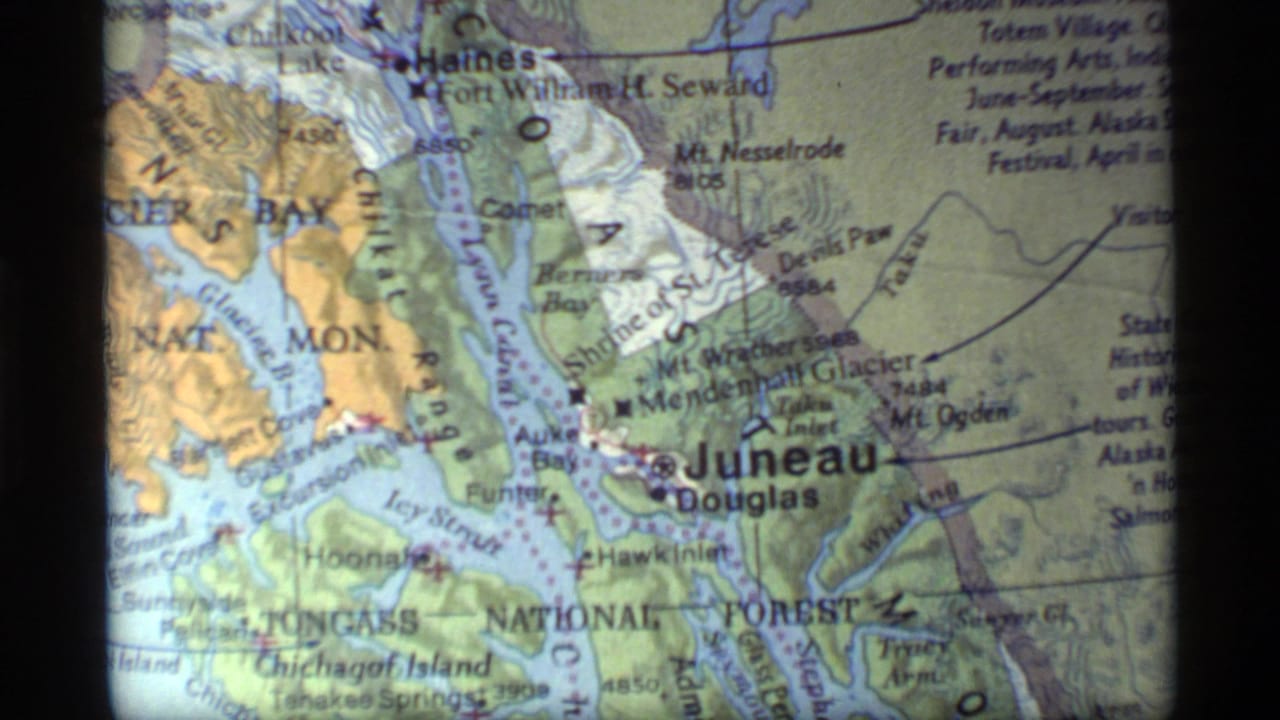 1977 8mm frame of a printed southeast Alaska map showing Juneau, Douglas, and nearby Glacier Bay area labels.
