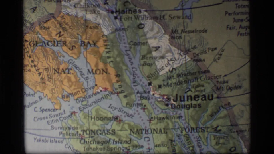 1977 8mm frame showing a projected Alaska regional map with Juneau, Douglas, Glacier Bay, inlets, and printed terrain markings.