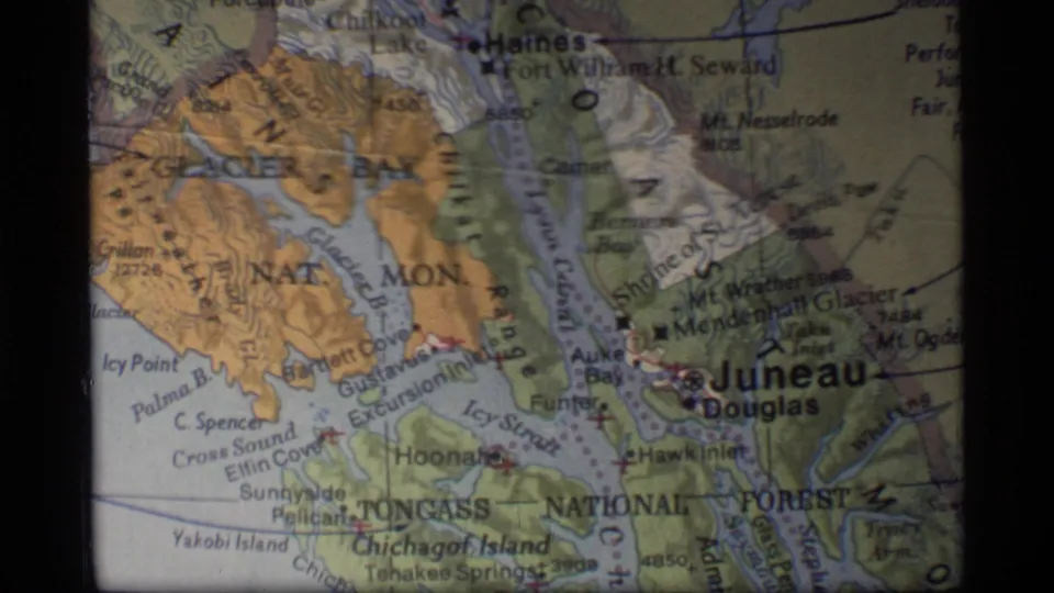 1977 8mm frame of a projected Southeast Alaska map with Glacier Bay, Tongass National Forest, Chichagof Island, and Juneau visible.