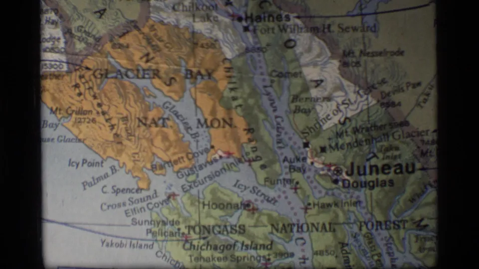 1977 8mm frame showing a projected regional map of Southeast Alaska with Juneau, Haines, Glacier Bay, and glacier terrain labels.