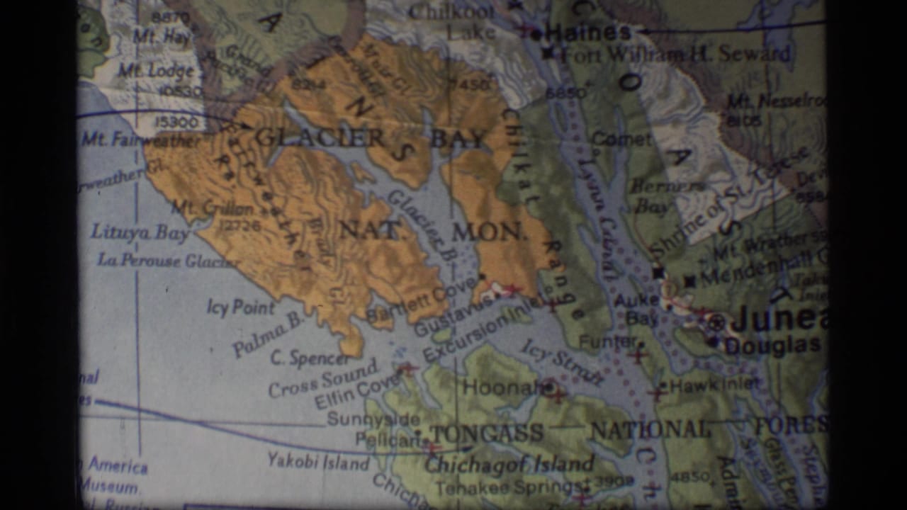 1977 8mm close-up of a Glacier Bay and Juneau area map, with Haines, Douglas, inlets, and terrain relief visible.