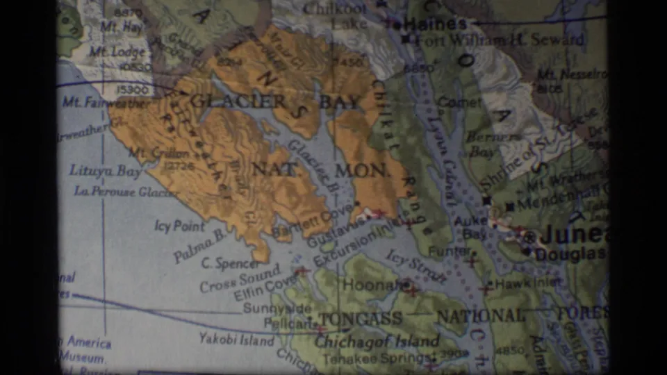 1977 8mm frame showing a printed map of Glacier Bay and the Juneau area with Icy Strait and island labels visible.