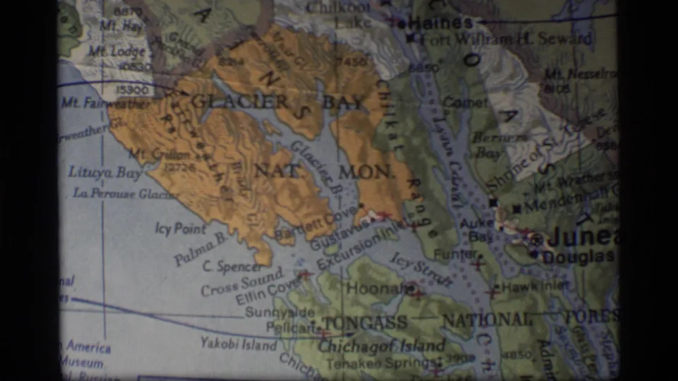 1977 8mm close-up of the Glacier Bay and Juneau region on a printed Alaska map, with waterways and mountain areas marked.