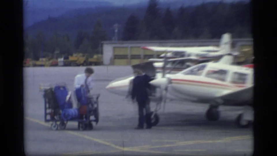 At Glacier Bay, Alaska in 1977, people and loaded luggage carts appear near a small white single-engine aircraft on the airport apron.