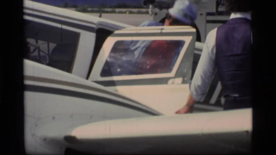 A close home-movie view shows people beside a small aircraft, with luggage visible inside or through the cabin window.