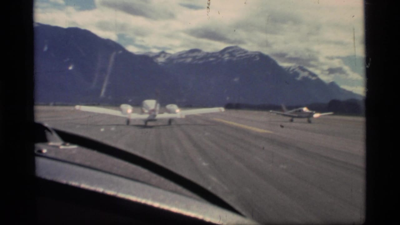 Small airplanes taxi on a runway with mountains in the background.
