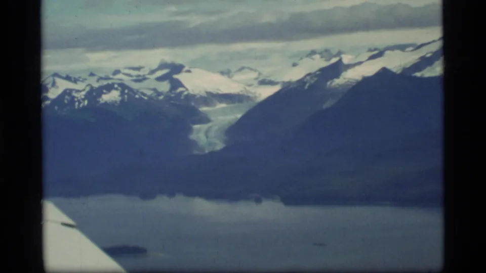 Glacier Bay, Alaska aerial view from 1977 with a glacier between mountain ridges, bay water below, and a white aircraft wing edge visible.