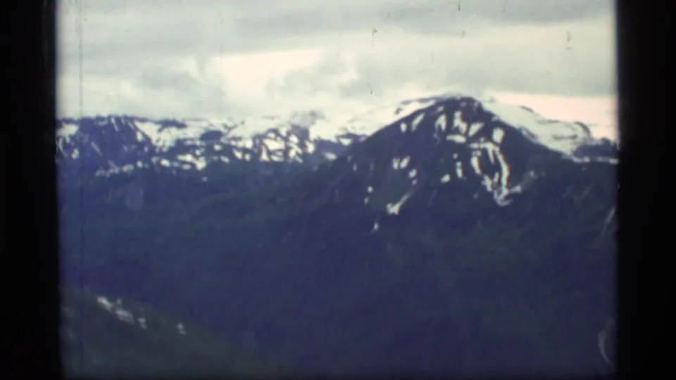 Aerial 8mm view of Glacier Bay mountain peaks with snow patches, filmed through a plane window in 1977.