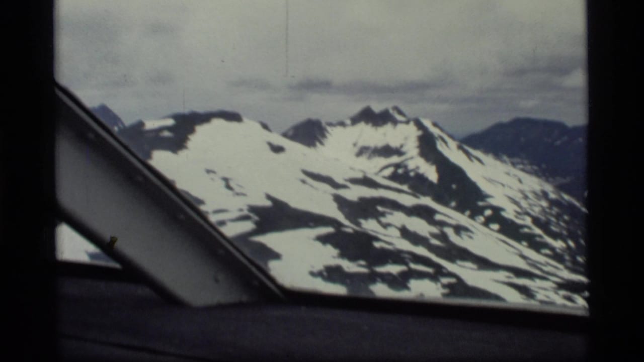 Snow-covered mountain peaks seen through an aircraft window frame.