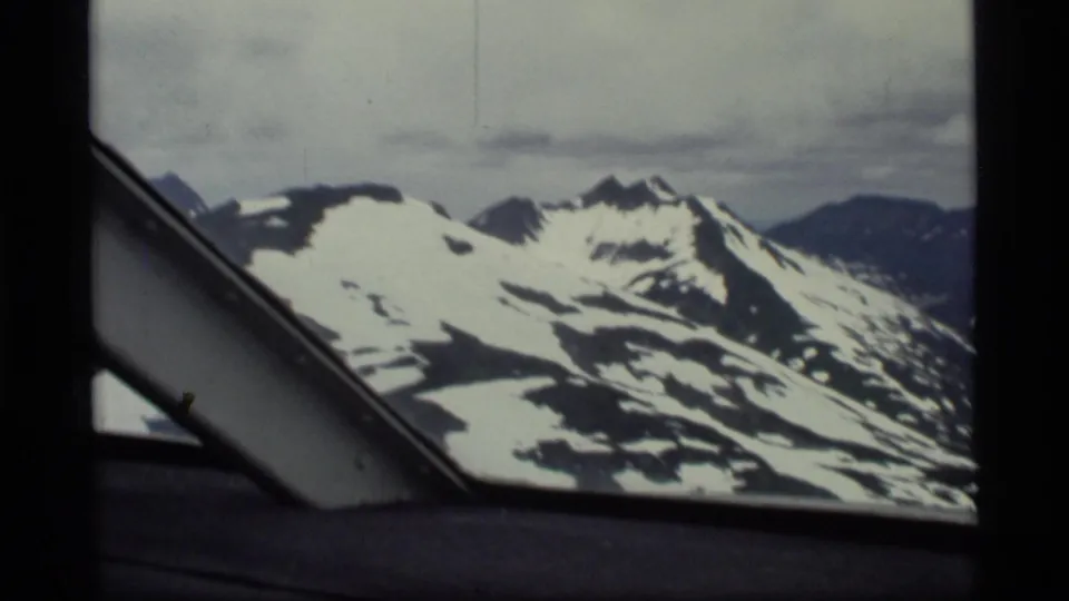 1977 Glacier Bay, Alaska 8mm frame showing snowy mountain ridges through the dark edge of an airplane window.