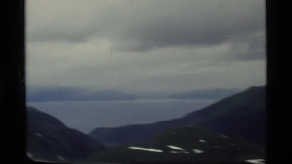 Glacier Bay, Alaska aerial view from a plane, showing blue-gray water between dark mountain slopes in 1977 8mm footage.