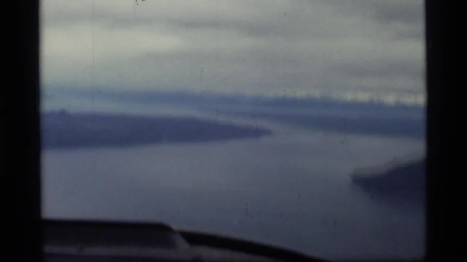 Blurred 1977 airplane-window view over Glacier Bay water and distant mountain ridges on 8mm film.