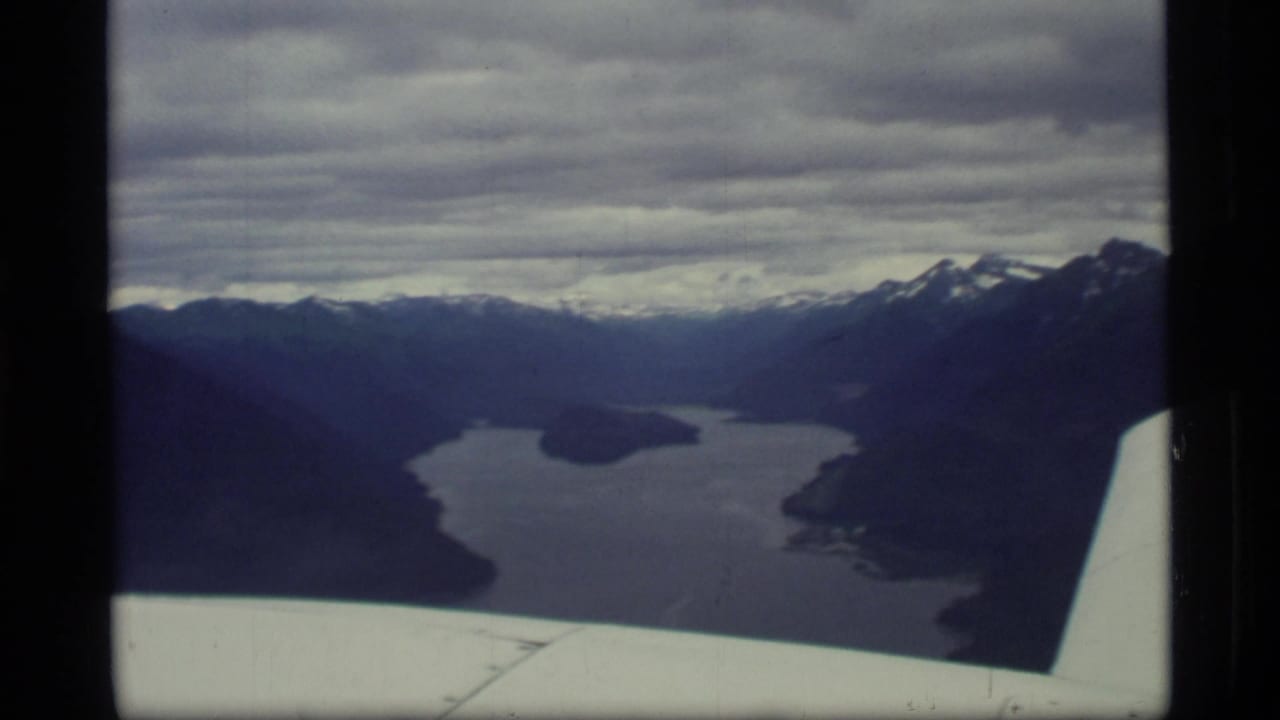 Aerial view of water between dark mountain ridges with an airplane wing in the foreground.