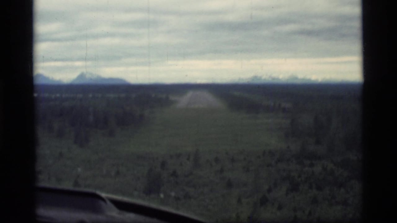 Runway seen through an aircraft window with forest and distant mountains ahead.