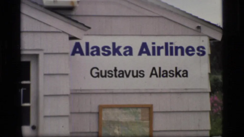 Close-up of the Alaska Airlines Gustavus Alaska sign on the terminal wall, with a framed map or notice beneath it.