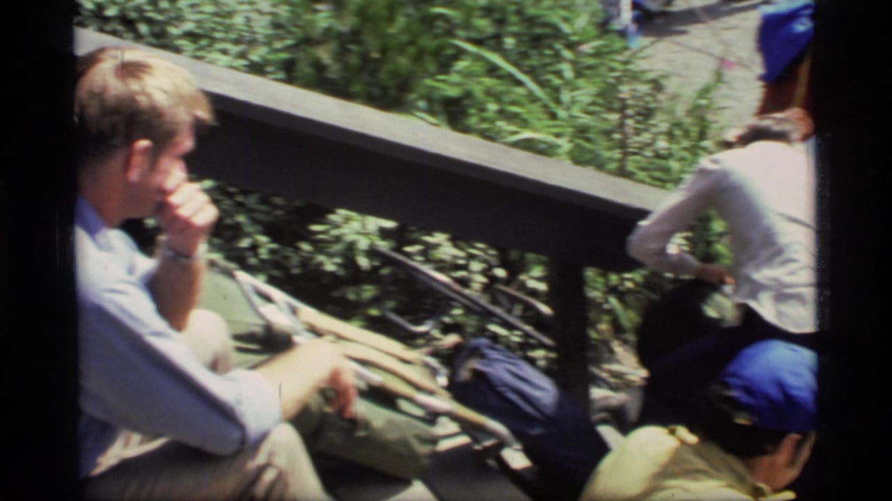 Hikers sit beside a wooden railing with backpacks and blue caps nearby.