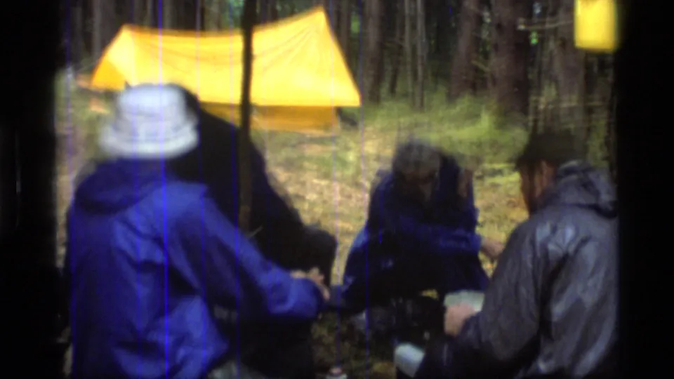 Closer 8mm campsite view with friends in jackets gathered near a yellow tent in the Glacier Bay forest.