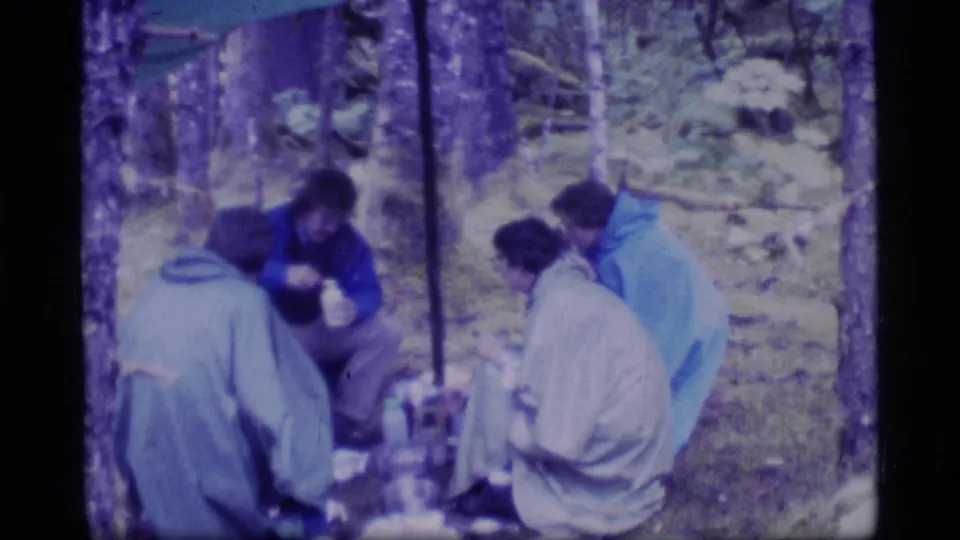 Four friends sit together on the forest floor during a 1977 Glacier Bay camping trip, seen in soft Super 8 color.