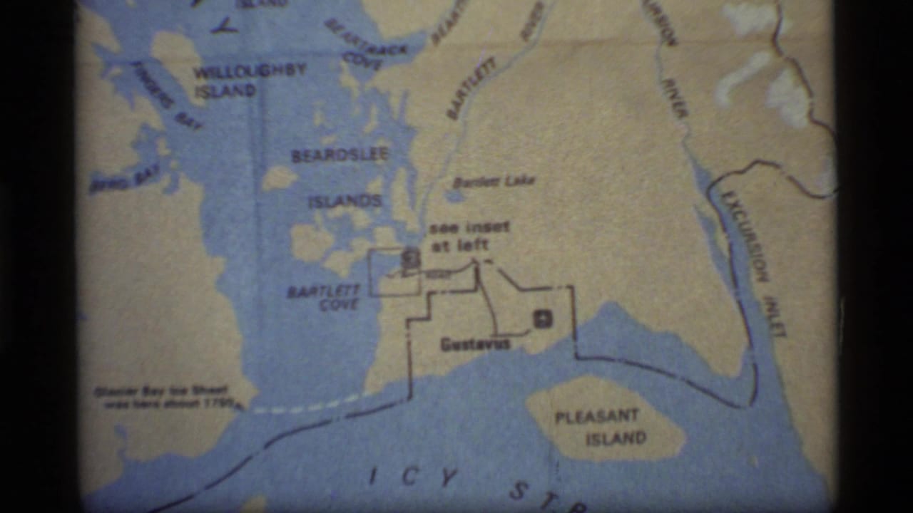 1977 8mm frame of a Glacier Bay area map with Bartlett Cove, Gustavus, Pleasant Island, and nearby waterways visible.