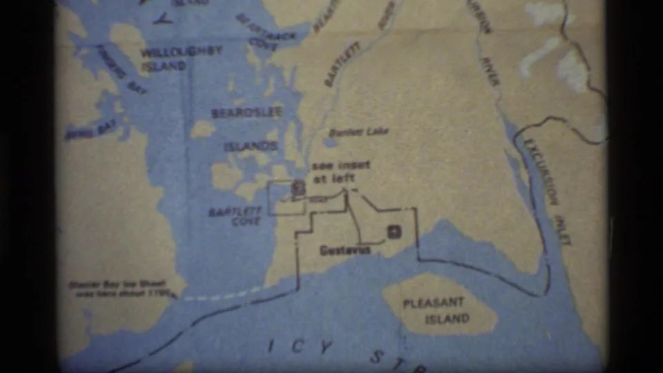 1977 8mm frame of a Glacier Bay area map with Bartlett Cove, Gustavus, Pleasant Island, and nearby waterways visible.