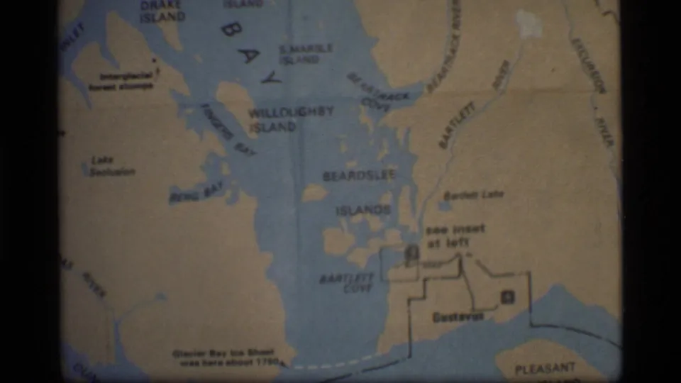 1977 8mm frame of a Glacier Bay map showing island names, Bartlett Cove, Gustavus, and a note near the lower left.