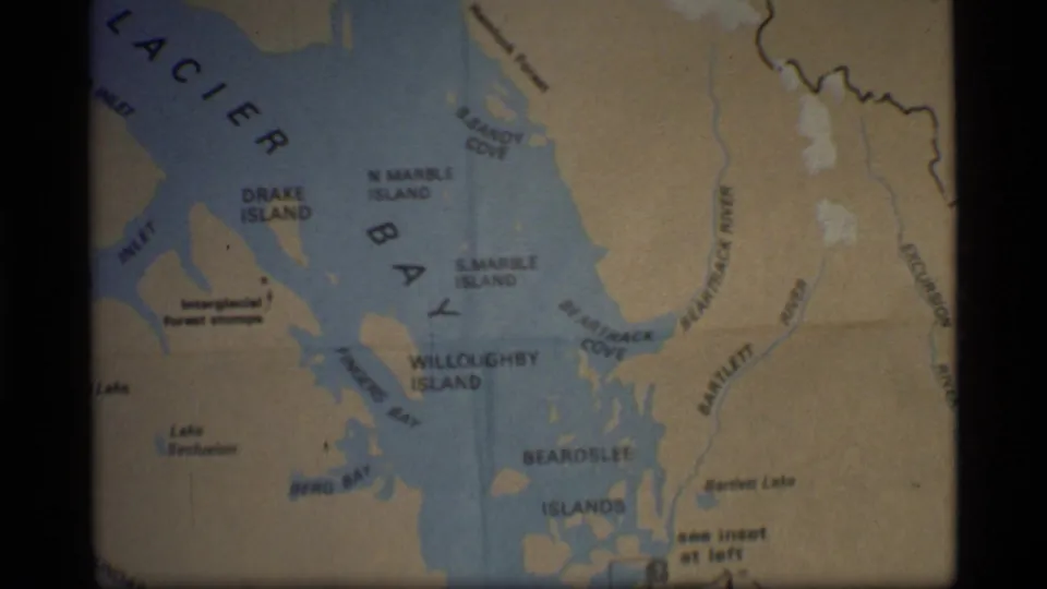 1977 8mm frame of the Glacier Bay map centered on island labels, blue water channels, and beige shoreline areas.