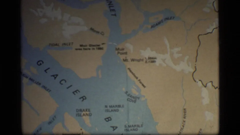Folded Glacier Bay, Alaska map in a 1977 home-movie frame, with Muir Inlet, Adams Inlet, and island labels visible.