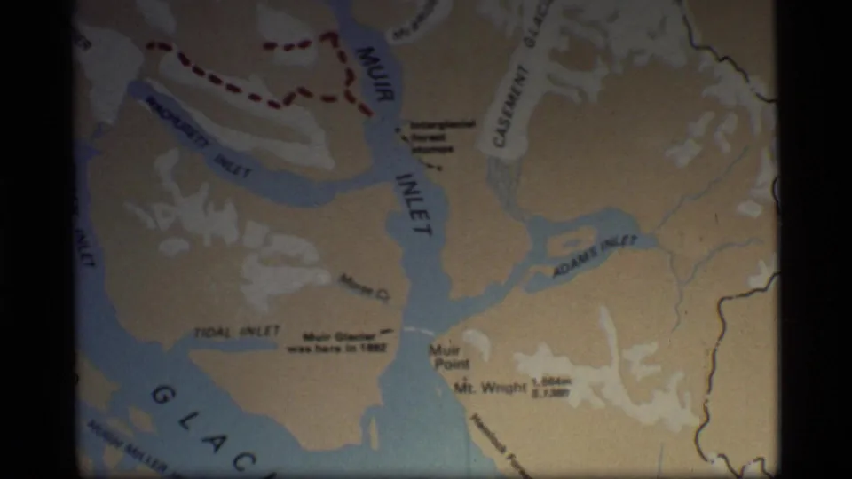 1977 8mm frame showing a printed Glacier Bay map, including Muir Inlet, Adams Inlet, Muir Point, Mt. Wright and blue inlet shapes.