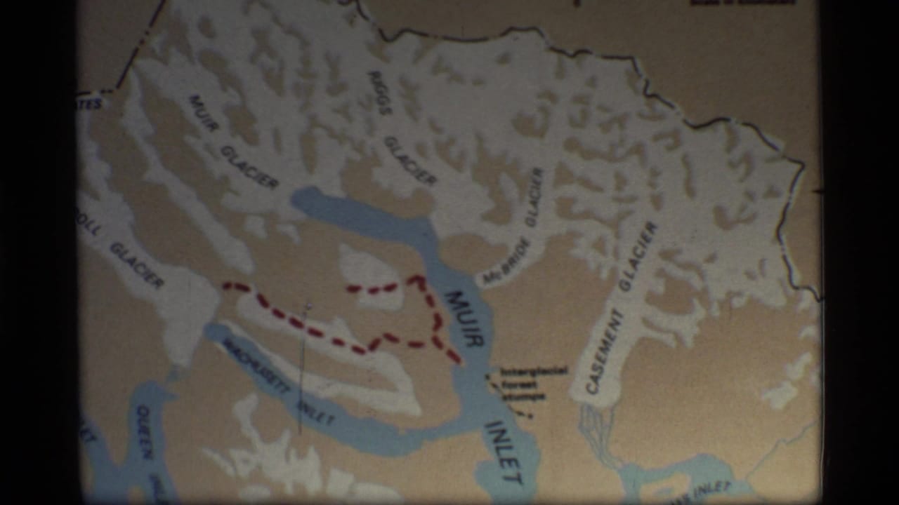 1977 8mm frame showing a Glacier Bay, Alaska map with glacier labels, Muir Inlet, and a red dashed route across the bay area.