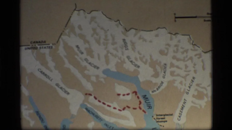 1977 8mm frame of the Glacier Bay map showing the Canada-United States boundary label, glacier names, waterways, and a dashed red path.