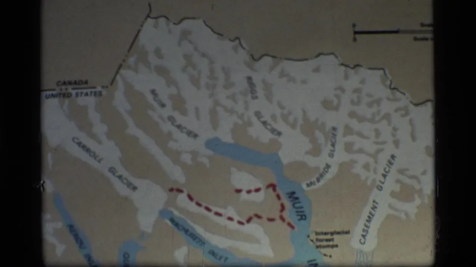 Glacier Bay, Alaska map in a 1977 home-movie frame, with border labels, glacier names, and a red dashed route visible.