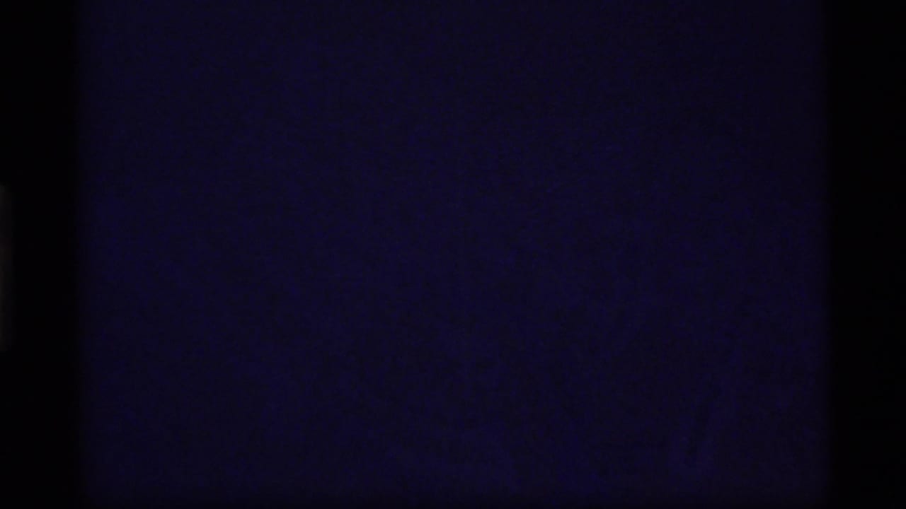 Dark opening 8mm frame from the Glacier Bay clip, with faint blue-purple exposure and heavy black film edges.
