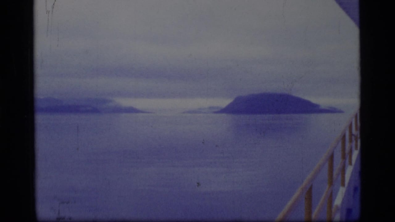 Calm water and distant dark landforms under cloudy sky, with a boat rail at right.