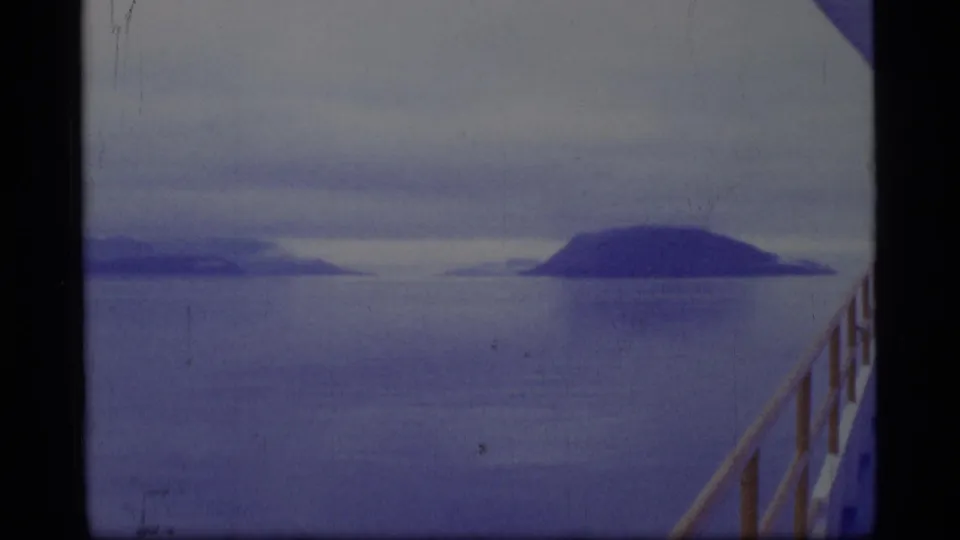 1977 8mm Glacier Bay boat view across blue-gray water toward distant islands or mountains beneath an overcast sky.