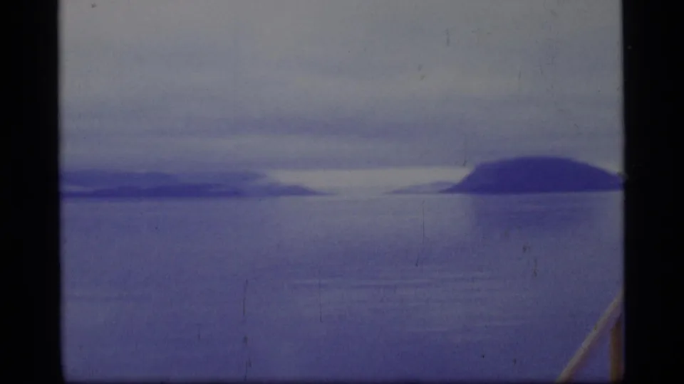 Glacier Bay scenery seen from a vessel, with blue-toned water, low clouds, and distant dark landforms in soft 8mm focus.