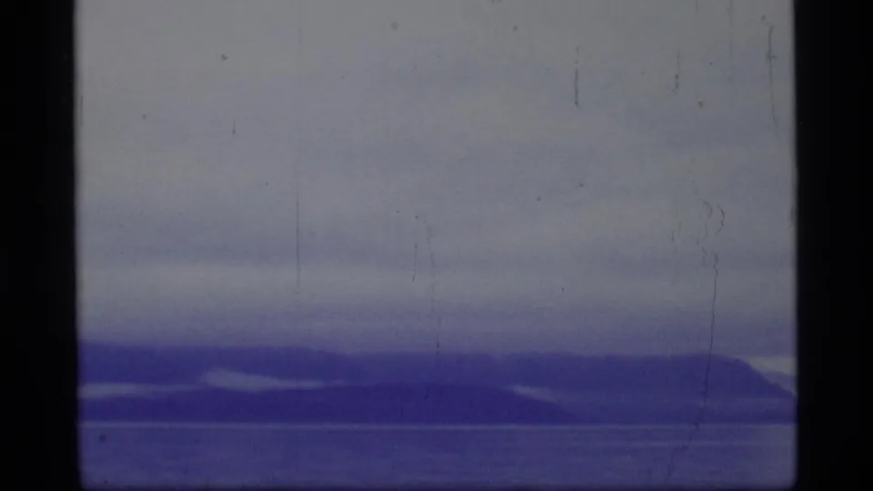 Blue-gray Glacier Bay landscape with overcast sky, distant shoreline or mountains, and visible 8mm film wear near the frame edges.
