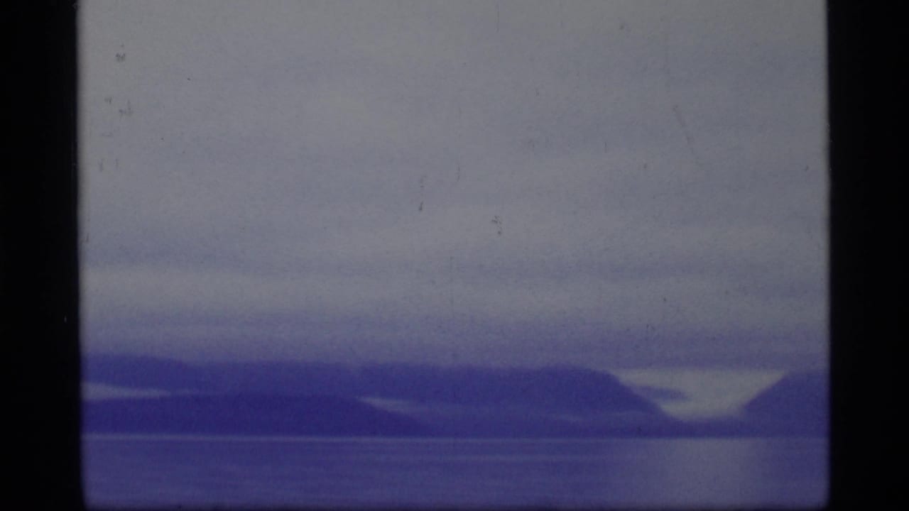 1977 8mm Glacier Bay view of still water and soft mountain silhouettes beneath a muted, cloudy sky.