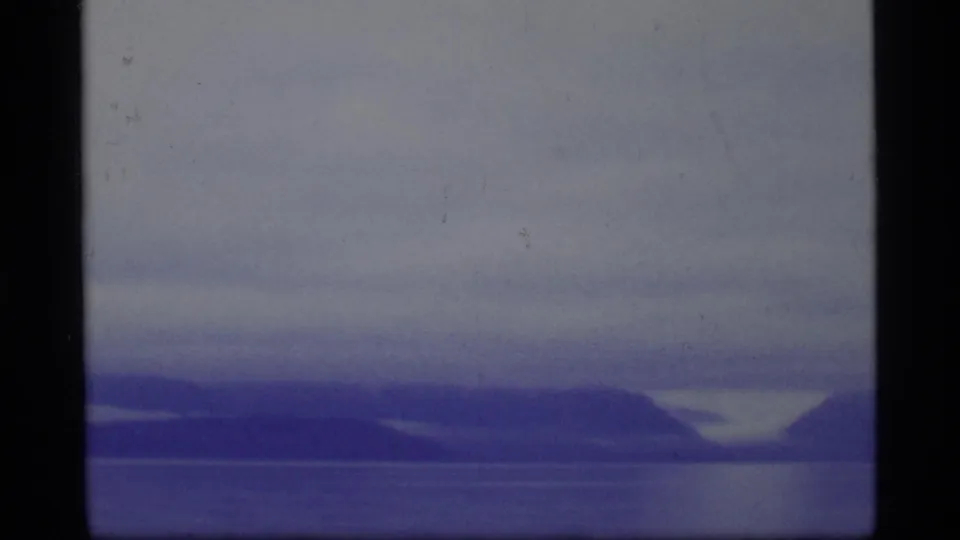 1977 8mm Glacier Bay view of still water and soft mountain silhouettes beneath a muted, cloudy sky.